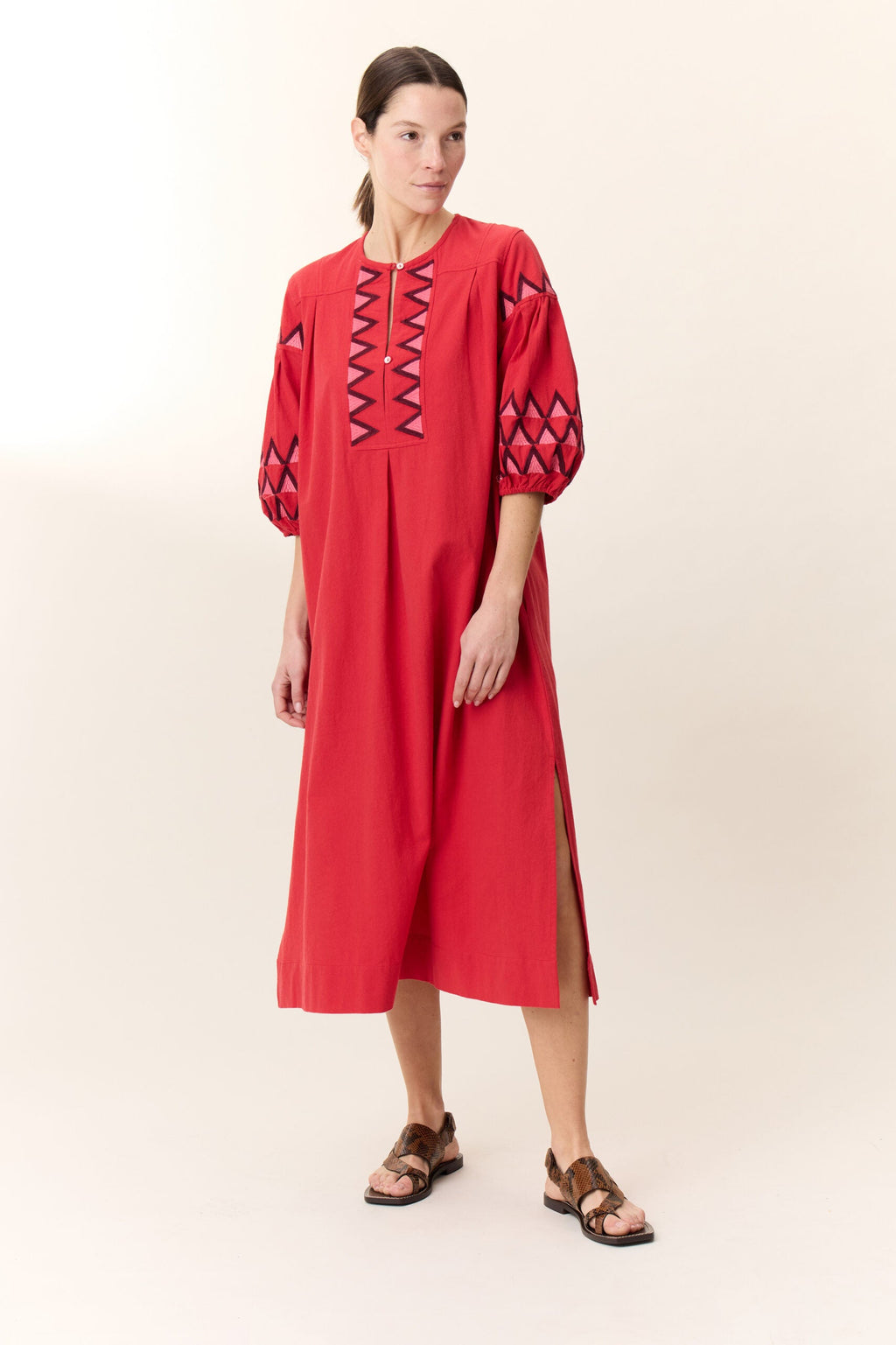 Robe Rudo Alpha – red cotton dress with geometric embroidery and ¾ sleeves, shown worn outdoors with a relaxed bohemian silhouette.